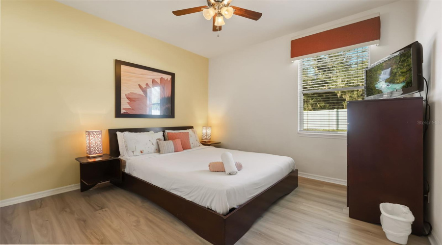 Comfortable queen guest bedroom featuring warm décor, laminate flooring, and a relaxing atmosphere.