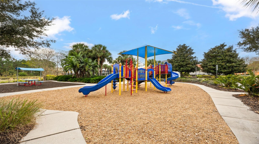 Community playground with shaded play equipment, picnic tables, and beautifully landscaped surroundings, offering fun for all ages.