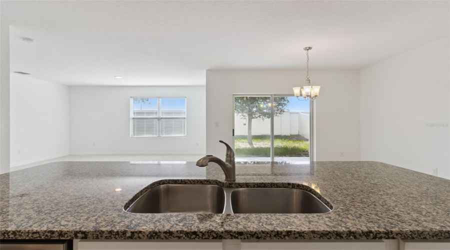 Island View & Open Sightlines:Central kitchen island featuring an undermount double-basin stainless steel sink with goose-neck faucet, looking out toward the sunlit dining nook and back patio.