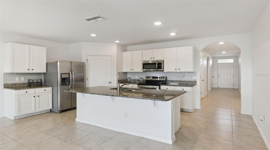 Kitchen:Well-appointed kitchen featuring a center island with sink, subway tile backsplash, dark granite counters, stainless steel appliances, and a pantry door.