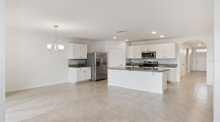Open-Concept Kitchen:Generous open-concept kitchen highlighting crisp white cabinetry, rich granite countertops, stainless steel appliances, and continuous tile flooring.