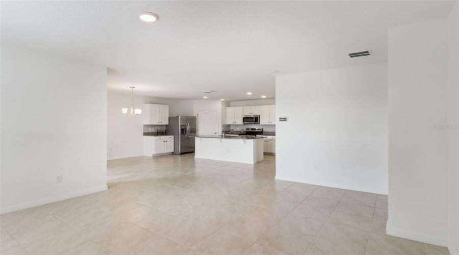 Open-Concept Main Living Space:Expansive open-concept floor plan combining the main living area and kitchen, featuring a central island, dark granite countertops, white cabinetry, and stainless steel appliances.