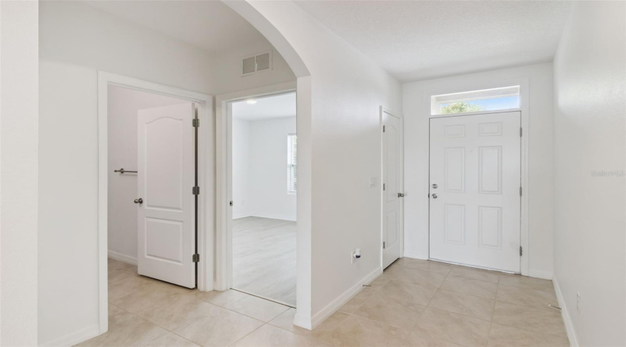 Foyer / Entryway:Bright and welcoming foyer featuring neutral tile flooring, crisp white walls, transom window natural light, and elegant arched doorways.