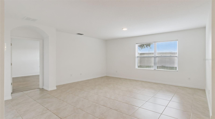 Flex Room / Formal Area:Spacious flex living space featuring continuous tile flooring, crisp neutral paint, and a large window filling the room with natural light.
