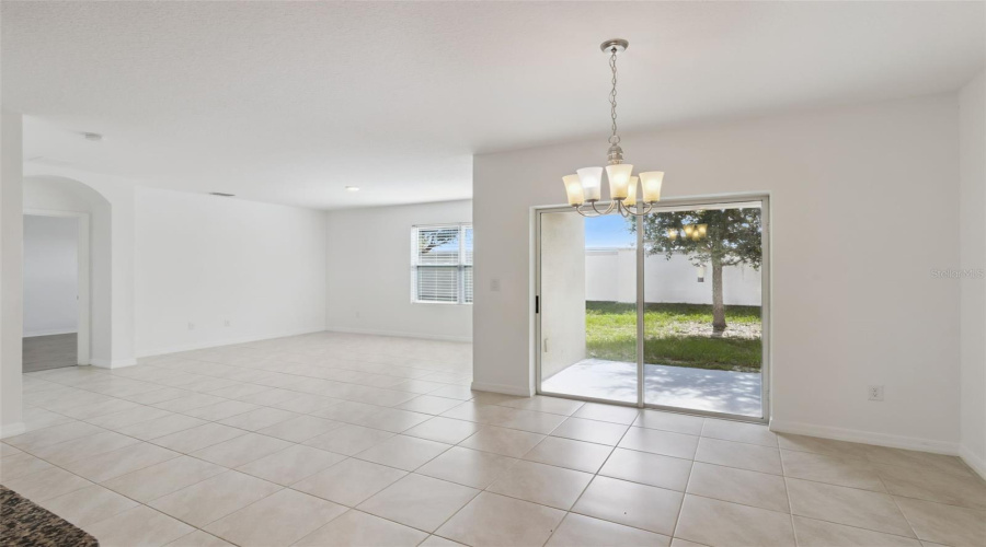 Dining Area & Patio Access:Bright dining space featuring neutral tile flooring, a timeless light fixture, and sliding glass doors leading out to the covered patio and backyard.
