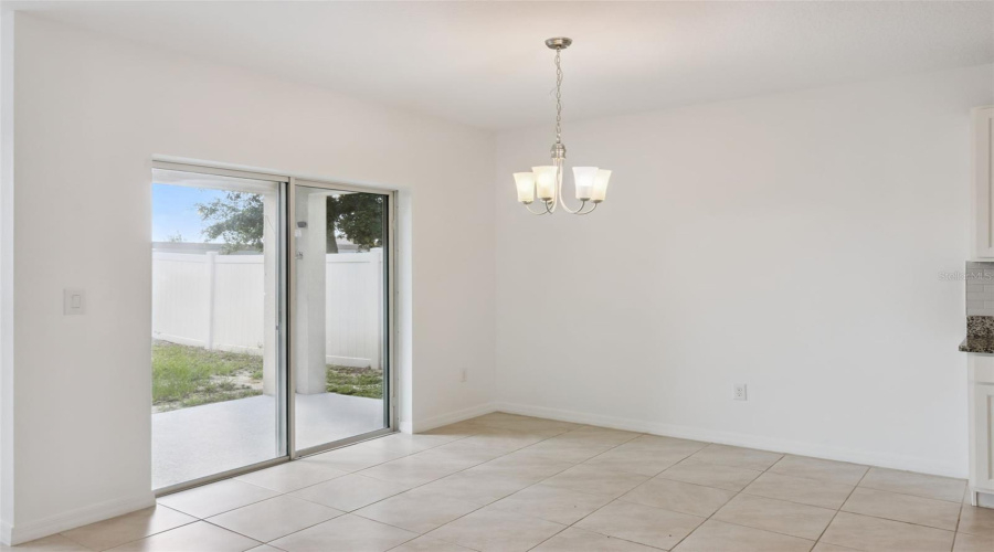 Dining Nook:Sunlit dining nook complete with an elegant chandelier, low-maintenance tile, and convenient glass slider access to the outdoor patio and fenced yard.