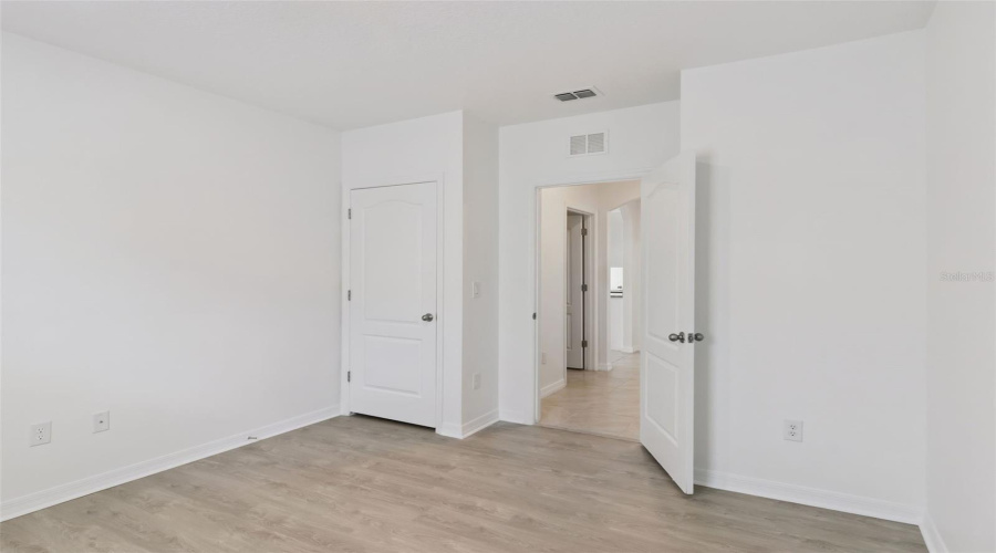 Spacious Bedroom Layout:Generous bedroom layout showcasing durable light wood-look flooring, clean white trim, closet, and easy access to adjacent hallway space.