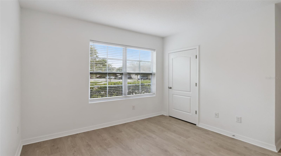 Sunlit Secondary Bedroom:Secondary bedroom offering low-maintenance wood-look flooring, fresh neutral paint, a private closet, and a large window with fitted horizontal blinds.