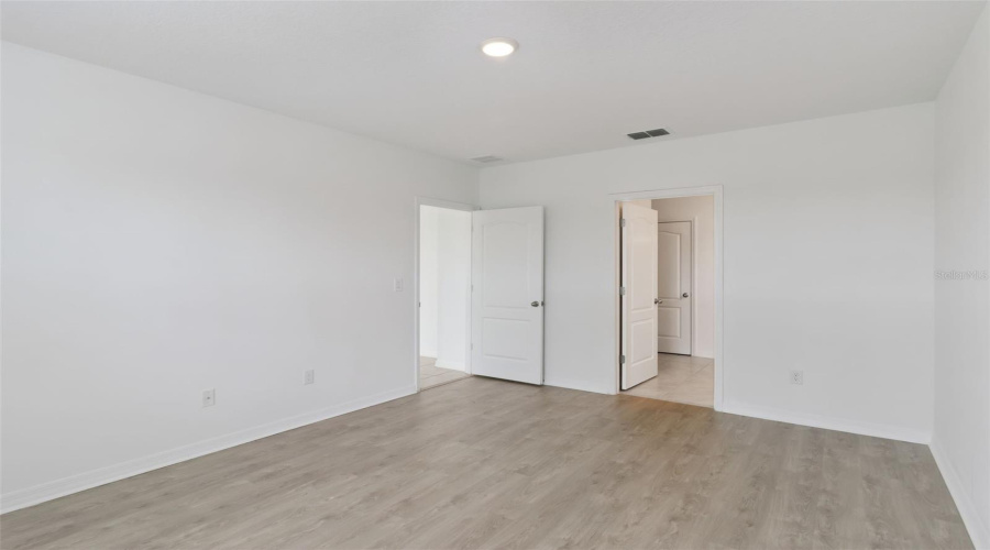 Primary Suite & En-Suite Access:Generous primary bedroom view showcasing smooth flooring transitions and dual doorways providing direct access to the en-suite bath and closet.