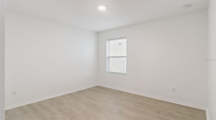 Bright Bedroom:Inviting secondary bedroom featuring pristine white walls, light wood-look plank flooring, and a fitted window offering bright natural light.