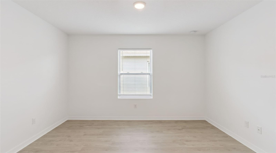 Centered Bedroom Layout:Symmetrical, light-filled bedroom with a centered picture window, fitted blinds, flush-mount lighting, and durable wood-look flooring.