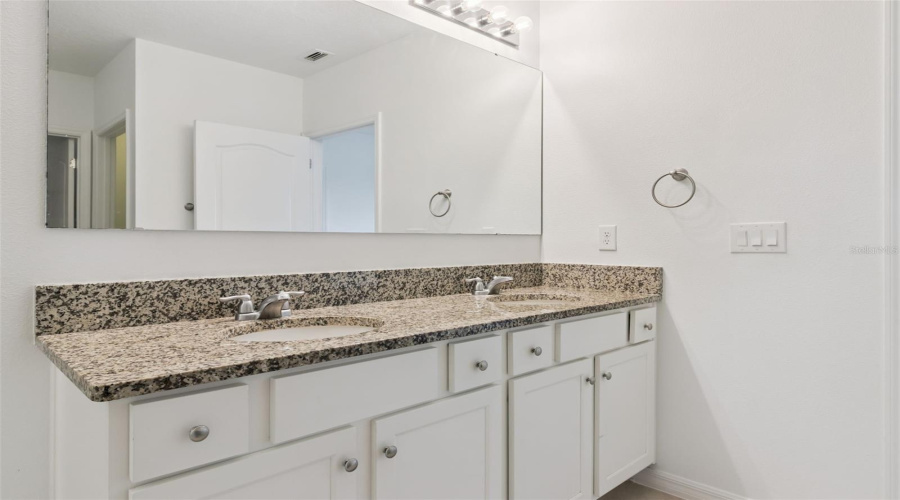Primary Bath Double Vanity:En-suite primary bathroom vanity featuring dual sinks, rich granite counter space, white cabinetry with silver hardware, and an expansive full-width mirror.
