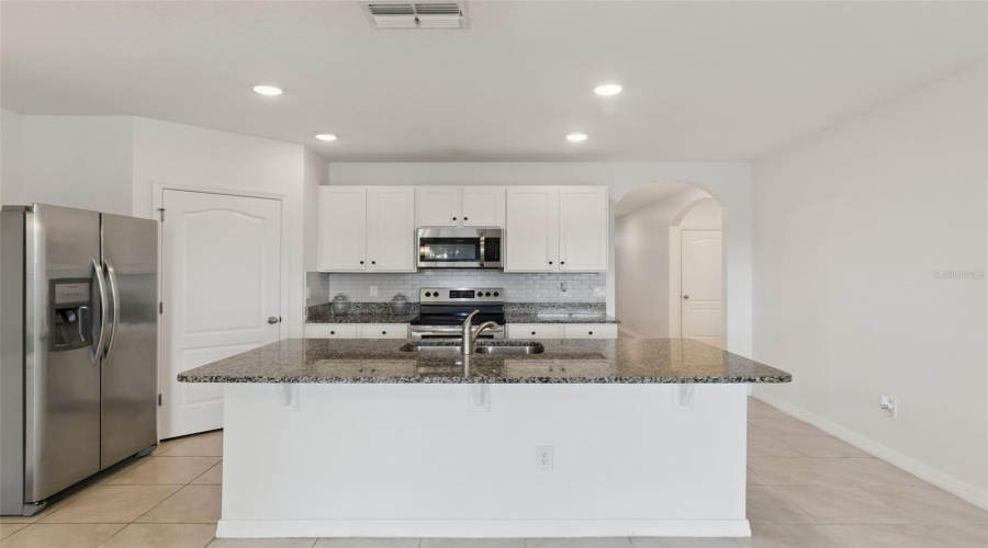 Kitchen Front Profile:Clean, symmetrical view of the kitchen highlighting the island prep area, white shaker-style cabinets, subway tile accent backsplash, and stainless steel appliances.