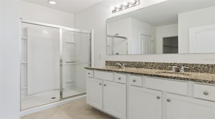Primary Bathroom & Walk-In Shower:Spacious primary bath highlighting a double-sink granite vanity, low-maintenance tile flooring, and a walk-in shower with framed glass sliding doors.