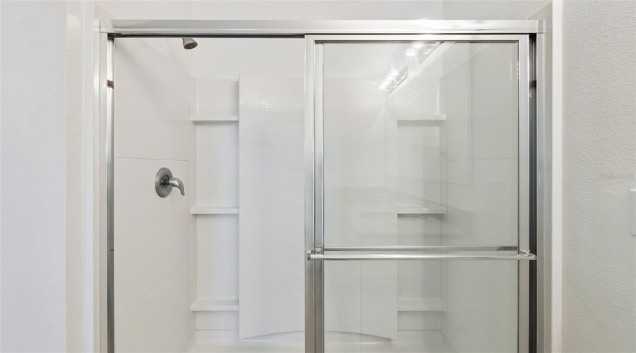 Walk-In Shower Detail:Spacious walk-in shower in the primary en-suite featuring chrome fixtures, built-in corner shelving niches, and sliding framed glass doors.