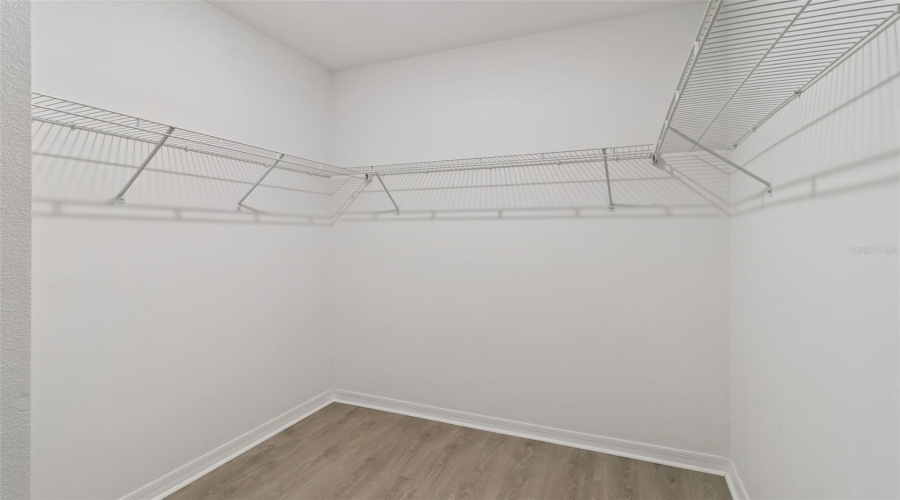 Walk-In Primary Closet:Generous primary walk-in closet outfitted with light wood-look flooring and multi-wall ventilated wire shelving for optimal storage organization.