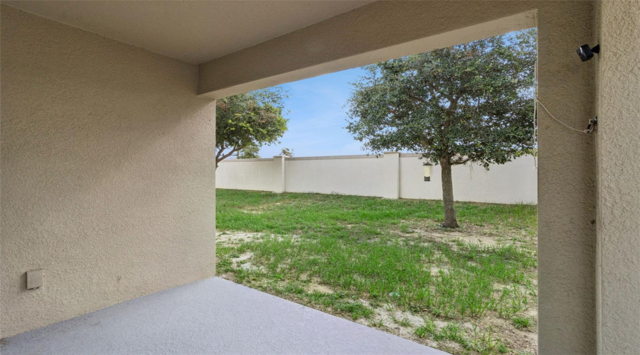 Covered Lanai View:Shaded covered lanai looking out toward a expansive grassy backyard with mature shade trees and a tall rear masonry privacy wall.