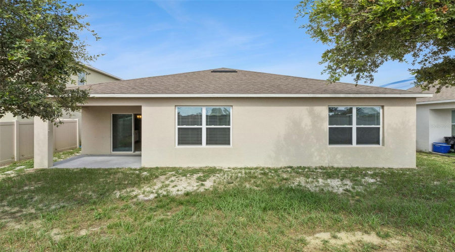 Rear Exterior Elevation:Single-story rear stucco elevation highlighting energy-efficient double-pane windows, a shaded rear patio alcove, and architectural shingle roofing.