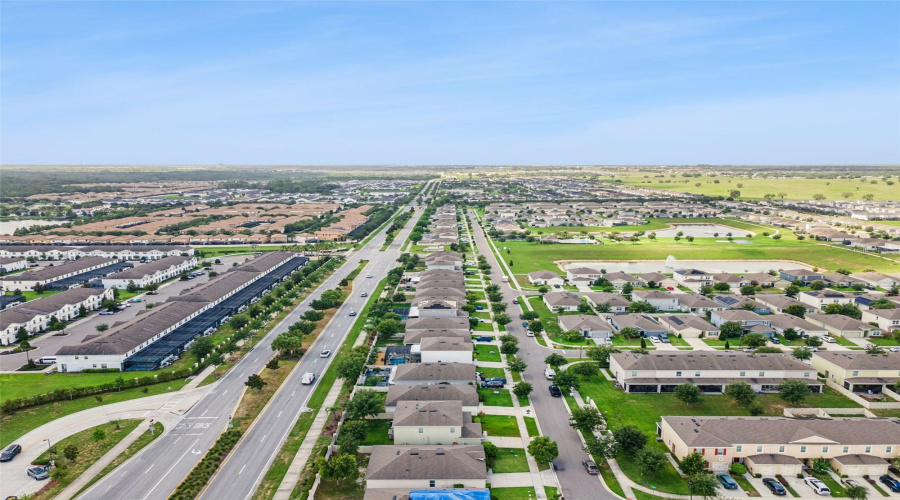 Community & Boulevard View:Elevated aerial shot featuring the beautifully landscaped main boulevard, neighborhood layout, and nearby community pond/water features.