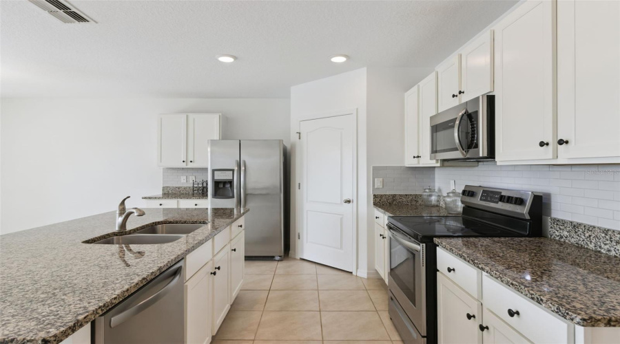 Kitchen Workstation:Detailed kitchen view showcasing generous granite counter space, electric glass-top range, built-in microwave, and functional cook prep areas.