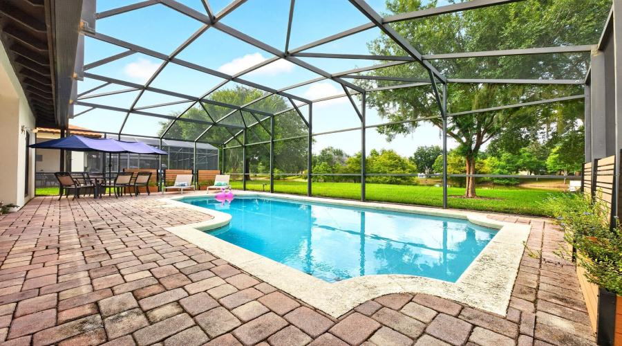 The SCREENED LANAI surrounds the HEATED IN-GROUND POOL with NEW POOL HEATER (2025) and NEW FILTER (2026) overlooking a generous backyard with peaceful POND VIEWS and no rear neighbors.