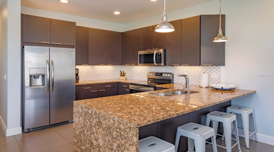 Alternate View Of The Modern Kitchen, Highlighting The Granite Countertops, Stainless Steel Appliances, Upgraded Cabinetry, And Breakfast Bar Seating.