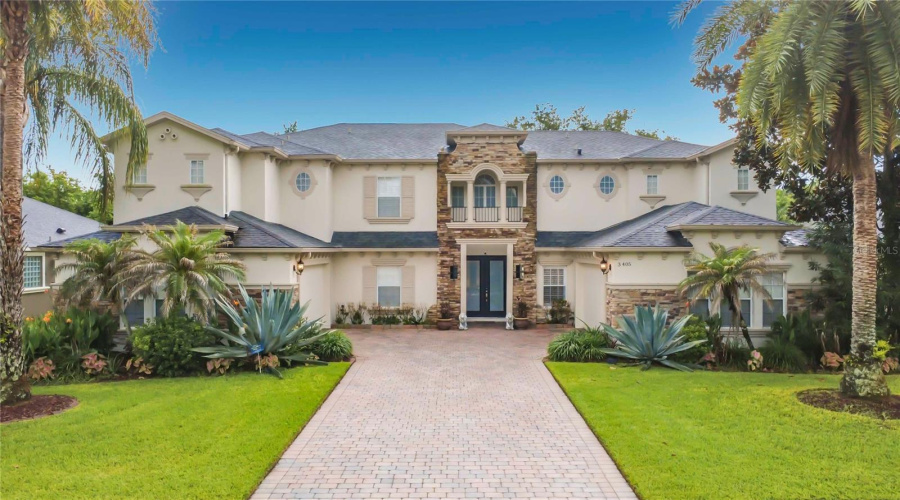 Exterior Front Of Residence. Double Door Covered Entry And Two 2-Car Garages Flanking Paver Driveway.