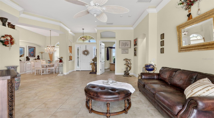 Expansive Formal Living Room Showcasing Double Tray Ceilings, Crown Molding, Tile Flooring Throughout, And An Open Layout Designed For Both Entertaining And Everyday Living.