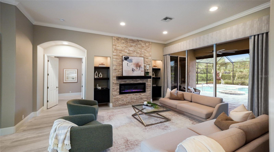 Updated Living Room Boasting 10’ Glass Doors With Voluminous Ceilings, Large Porcelain Tile Flooring, And A Fireplace Stone Accent Wall