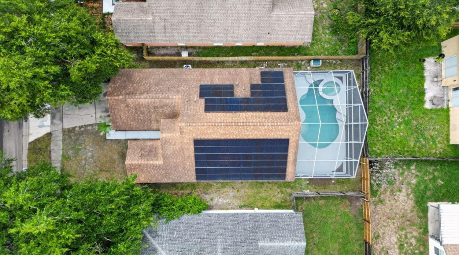 Aerial View Of The Home Featuring Rooftop Solar Panels And A Screen-Enclosed Pool.