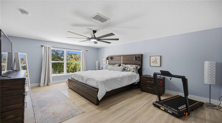 Primary Bedroom Has Large Windows For View Of Green And Wooded Backyard