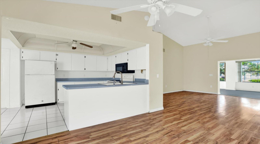The Kitchen, With White Cabinets, Tile Flooring, And An Open Line Of Sight To The Living Room.