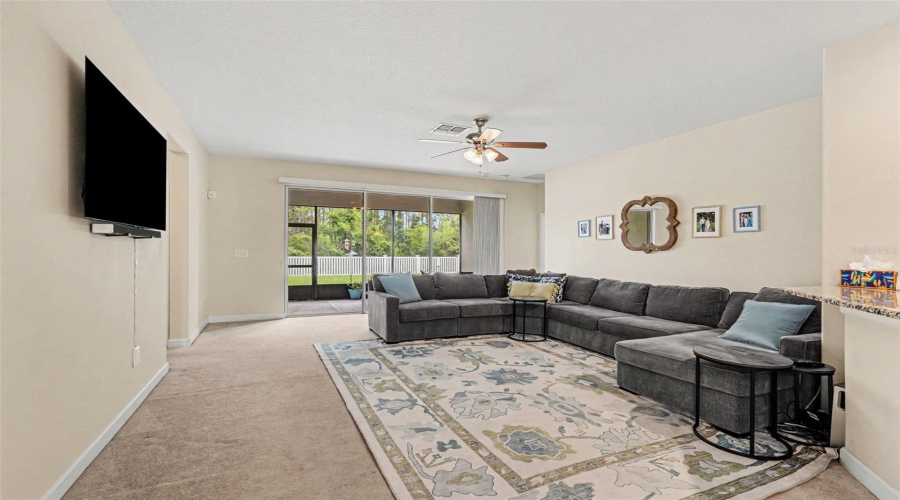 Bright Family Room With Oversized Sectional, Ceiling Fan, And Sliding Glass Door Opening Directly To Screened Lanai And Backyard In Tampa Fl 33647. 2 Bedrooms &Amp; Full Bath To The Far Left, Primary Suite To The Far Right
