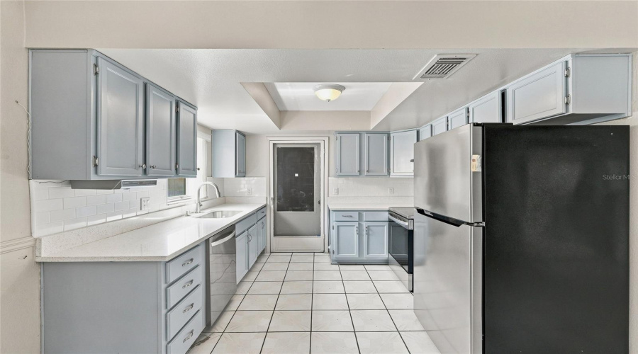 Galley Kitchen Featuring Light Blue Cabinetry, White Tiled Flooring, Stainless Steel Appliances, And White Countertops