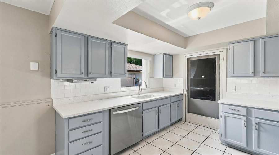 Kitchen With Light Gray Cabinetry, White Countertops, Subway Tile Backsplash, And A Stainless Steel Dishwasher
