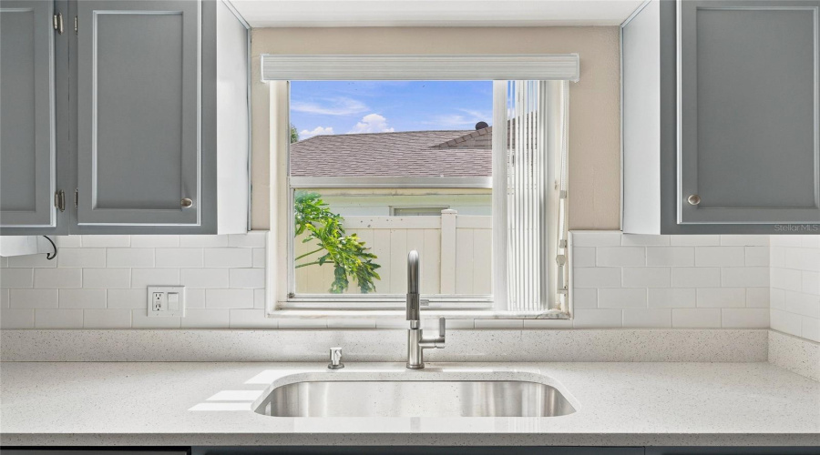 Stainless Steel Sink With A Gooseneck Faucet, Light-Toned Countertop, Subway Tile Backsplash, And Light Gray Cabinetry