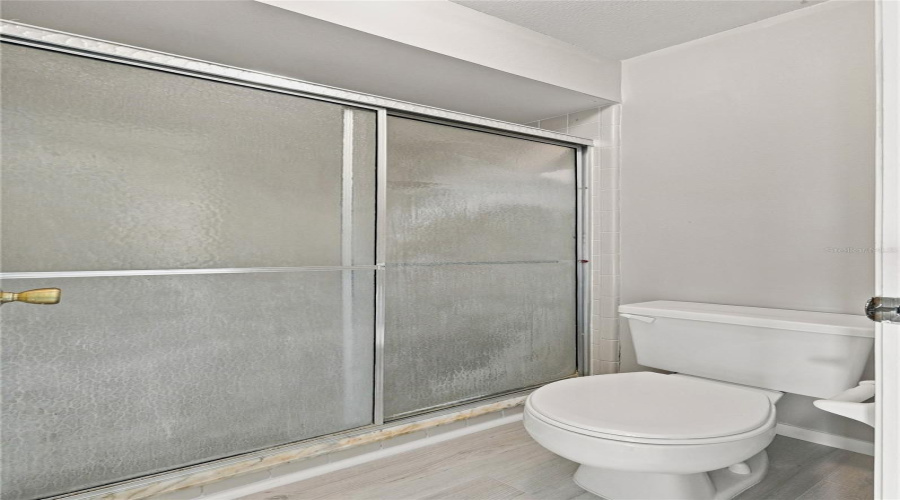 White Toilet With A Built-In Toilet Paper Holder And A Shower With Sliding Frosted Glass Doors