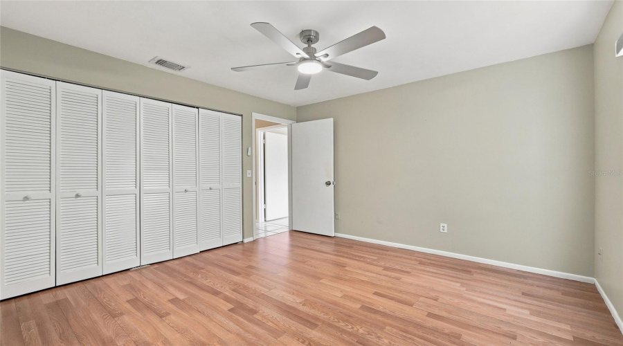 Wood-Finish Flooring, Ceiling Fan With Integrated Lighting, Louvered Bi-Fold Closet Doors, And Neutral Wall Paint