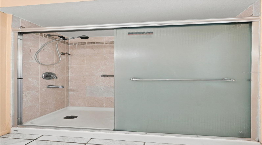 Modern Frameless Glass Shower Enclosure Featuring A Sliding Glass Door With Frosted Panel, Chrome Hardware, And A Spacious Walk-In Layout