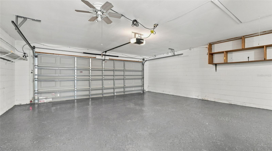 Concrete Flooring, White Shiplap Walls, Wood Shelving, Ceiling Fan, And Garage Door Opener
