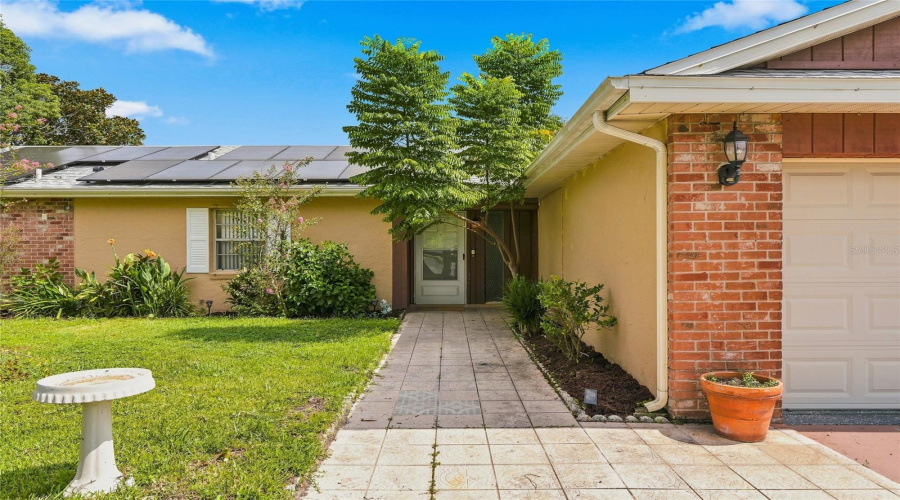 Exterior Featuring Solar Panels, Brick Accents, A Paneled Garage Door, And A Tiled Walkway