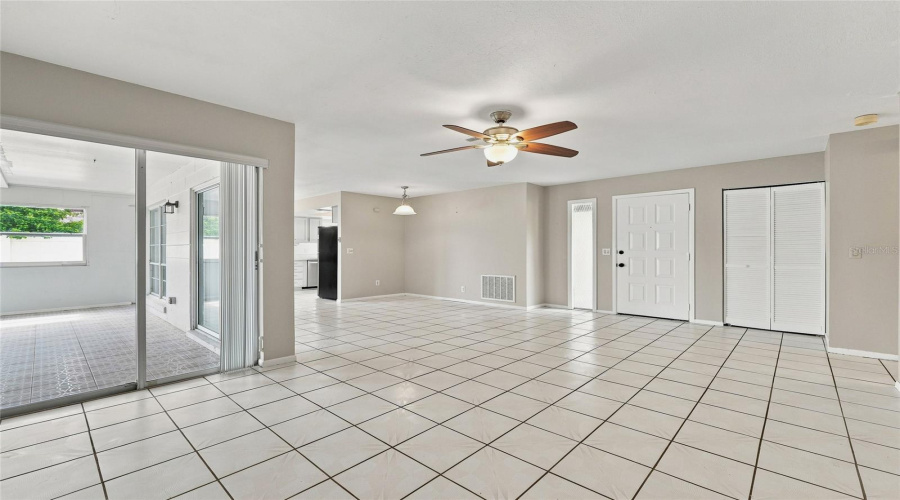 Spacious Open-Concept Living Area Featuring White Tile Flooring, A Ceiling Fan With Integrated Lighting, And A White Paneled Entry Door