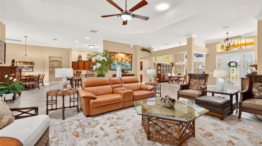 Another View Of The Living Room - Showcases Upscale Furniture Pieces In The Lr Seating Configuration - 1) &Quot;Key Largo&Quot; Side Tables &Amp; Cocktail Table W/ Glass Top (Front), Part Of Island Estate Collection (Front L, Center Front, &Amp; R) And 2) &Quot;Rum Beach Chairs&Quot;, Rattan High Back Wing Chairs (R),  Part Of Bali Hai Collection, 3) Brown Leather Ottoman, And 4) &Quot;Bimini Square End Table&Quot; - All Manufactured By Tommy Bahama Home. Note The Background Locations Of The Breakfast Nook (Back Far L), Adjacent Kitchen (Center Back -Partially Visible), Formal Dining Room (Back R) And Foyer (Far R).