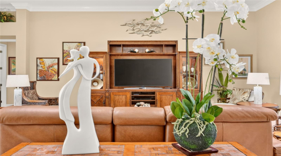 Living Room - Close-Up View Of Wall Entertainment Center W/ Shelving And Glass Cabinetry As Well As Decor Items Of Dancing Couple Statue &Amp; Large Artificial Orchid Arrangement On Sofa Table Behind The Natuzzi Leather Reclining Love Seat.