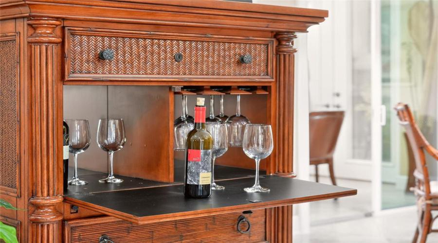 Located On Perimeter Of Breakfast Nook Area, This Tropical Style Drop-Front Dry Bar Cabinet, Manufactured By Broyhill Furniture, Features A Fold-Down Serving Surface, Mirrored Back, Stemware Rack, Bottle Storage And A Woven Rattan Tropical Design