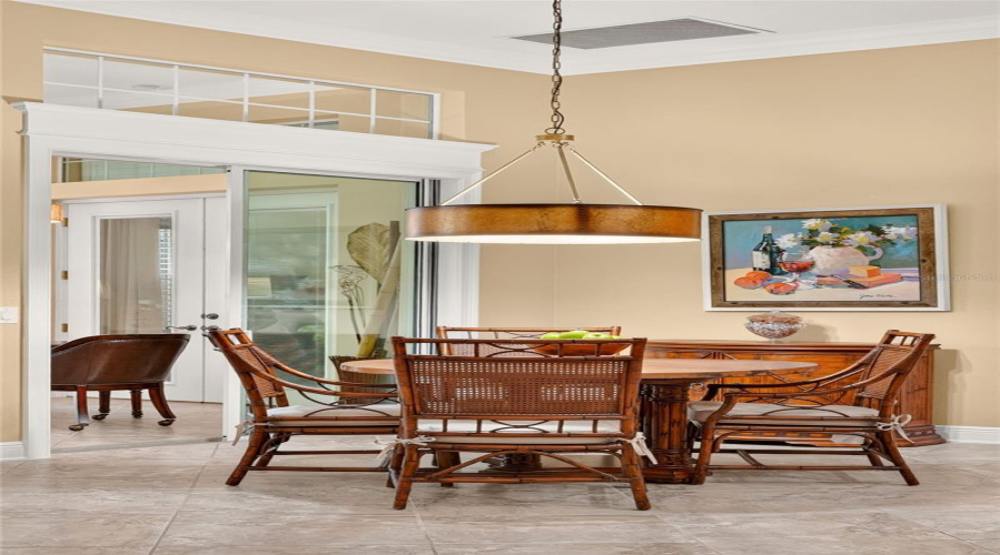 View Of Breakfast Nook - Shows A Large Circular Pendant Light Hanging Over A Tommy Bahama Home Rattan Dinette Set W/ Round Pedestal Table And 4 Cane Back Chairs. A Demilune Console/Buffet Table, Manufactured By Broyhill Furniture, Is Located Behind The Dinette Set.