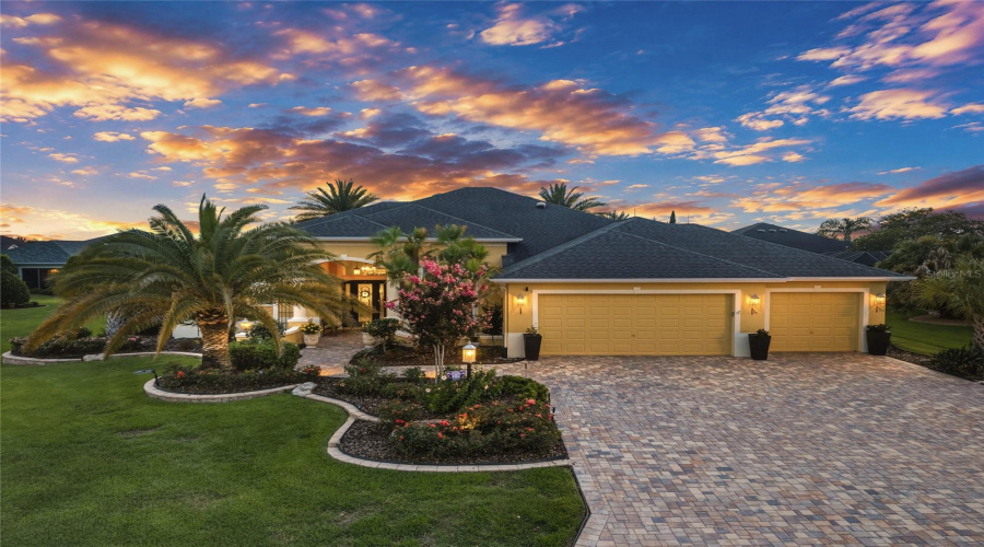 Front Exterior @ Dusk (Low Aerial View) - Note The Arch Shingle Hip Roof Line Against The Sky And The 3 Car Garage W/ Extra Width Of The Pavered Driveway.