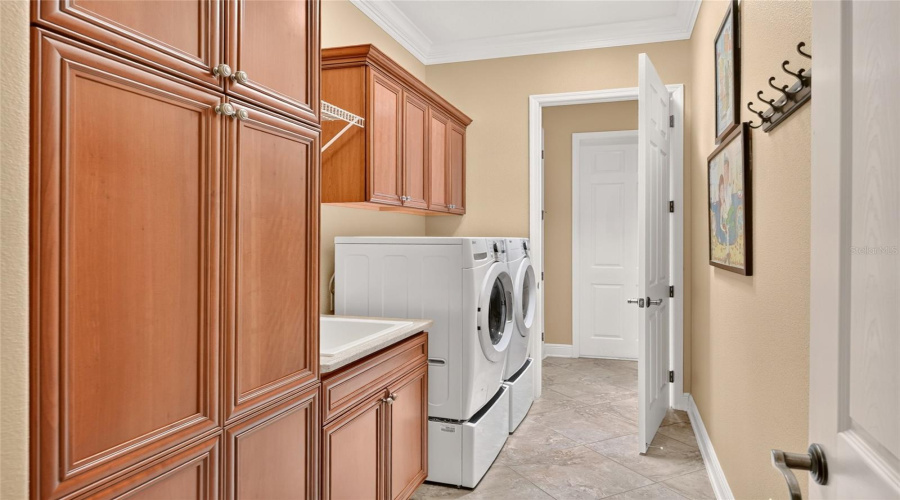Interior Laundry - View Of Hallway From Kitchen &Amp; Primary Suite Leading To Interior Laundry With Doors At Both Ends. There Is Plenty Of Extra Cabinet Storage, A Laundry Sink, And A Front Load Washer &Amp; Dryer Set.
