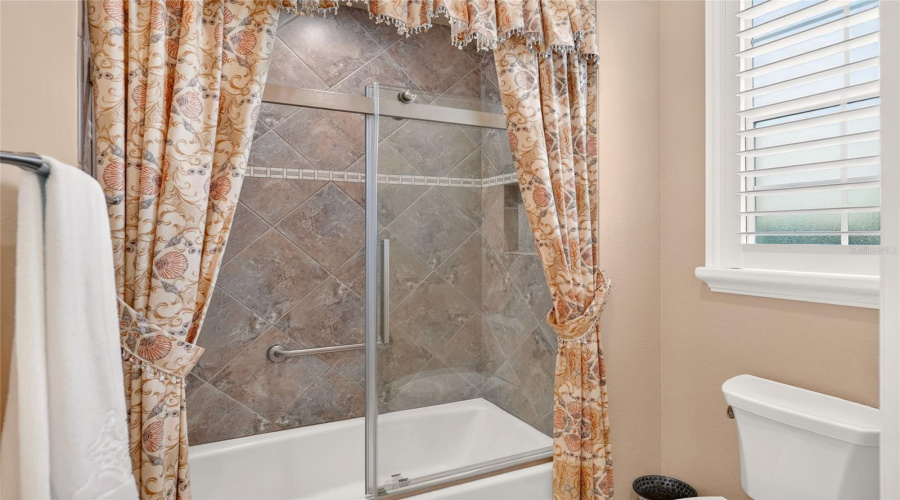 Bathroom #2 - Close-Up View Of Tub/Shower W/ Sliding Shower Glass Door. Window W/ Plantation Shutters Provides Natural Light. Pocket Door Provides Private Area To Tub/Shower Combo And Comfort Height Toilet.