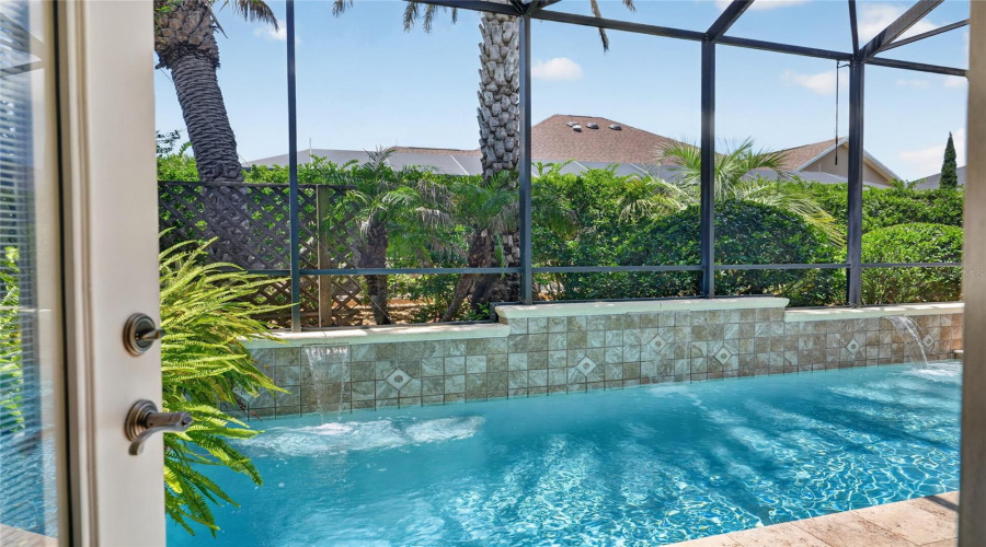 View Of Pool- First Glimpse Through The Doorway Of Bathroom #3 Reveals The Mansard Screen Enclosed Pool Area W/ A Raised Decorative Tiled Wall W/ 3 Cascading Water Falls. Lush Tropical Landscaping W/ Palm Trees Provides Privacy.